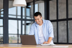 Successful professional using laptop for work standing in the modern office, smiling
